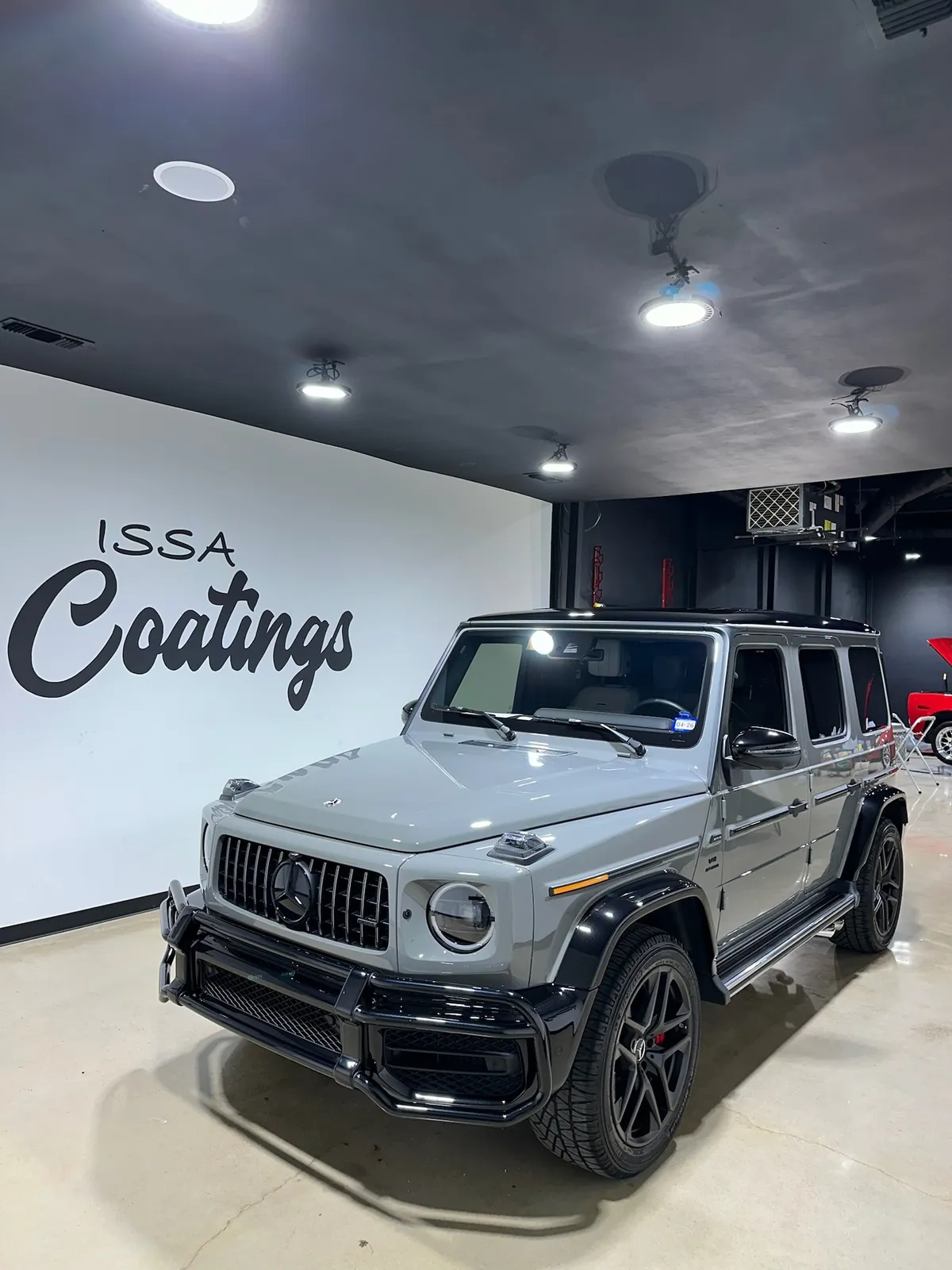 Silver Mercedes-Benz G-Class beside the ISSA Coatings wall logo