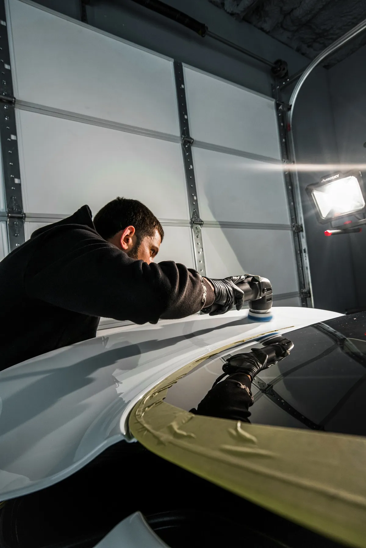 A technician polishing a white car with the trim masked off