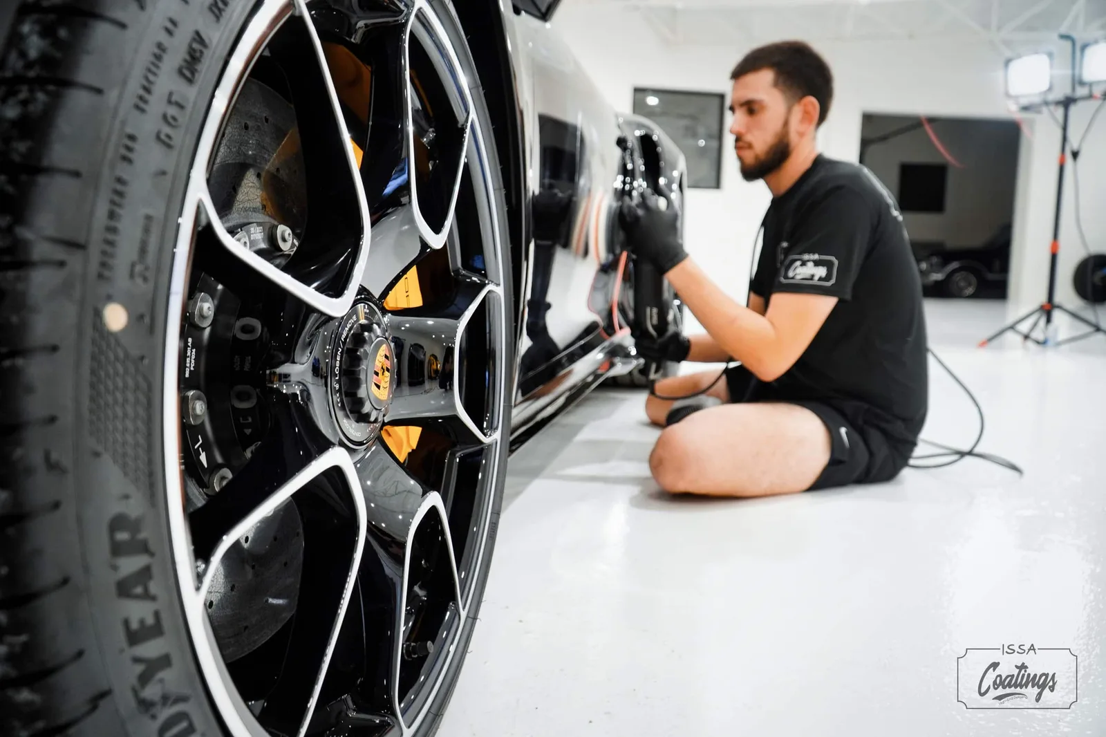 An ISSA Coatings technician polishing a black Porsche in the workshop